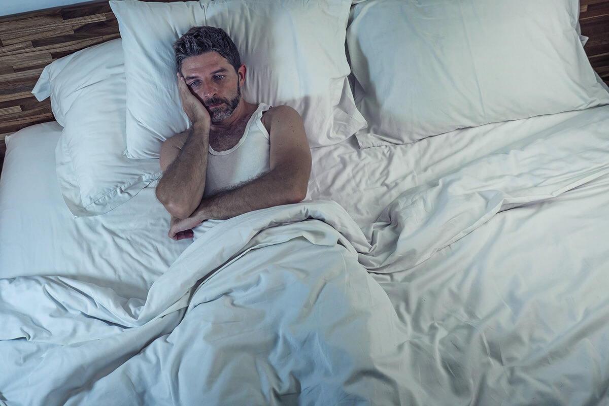 a man lies in bed and considers alcohol withdrawal symptoms