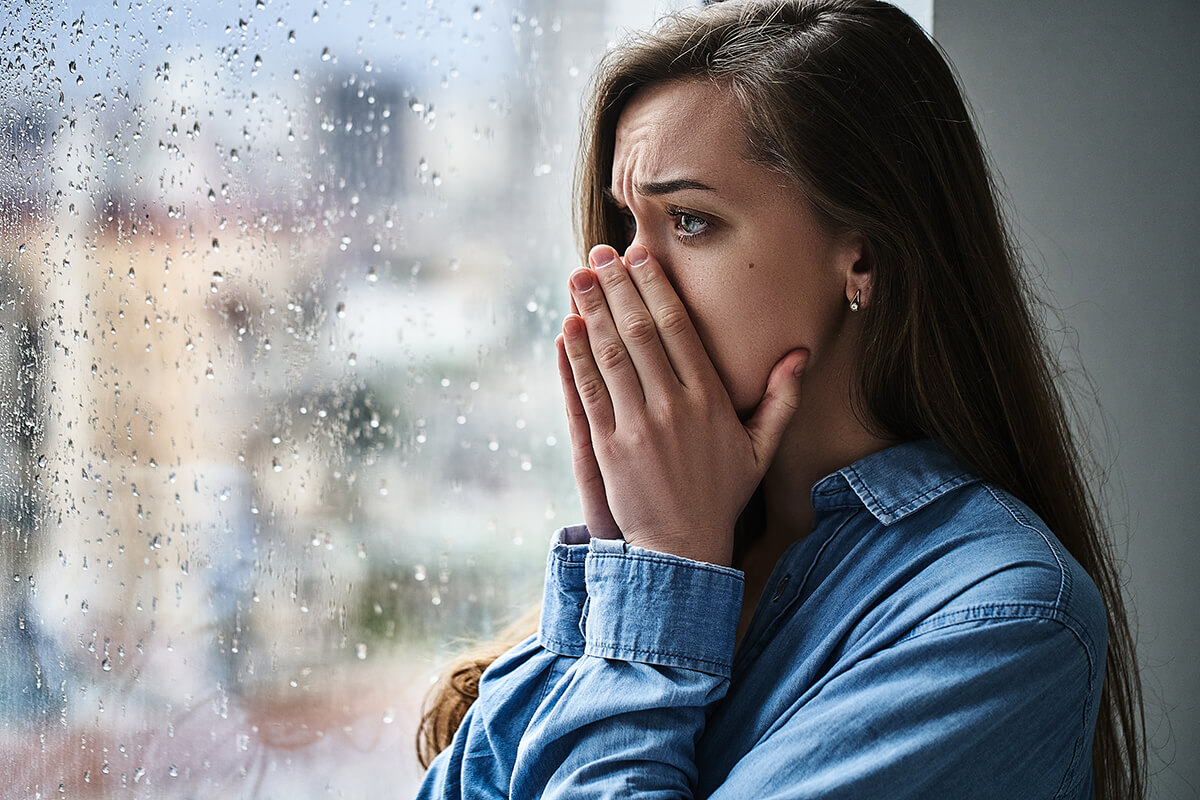 a woman stares out the window on a rainy day as she considers drug overdose symptoms