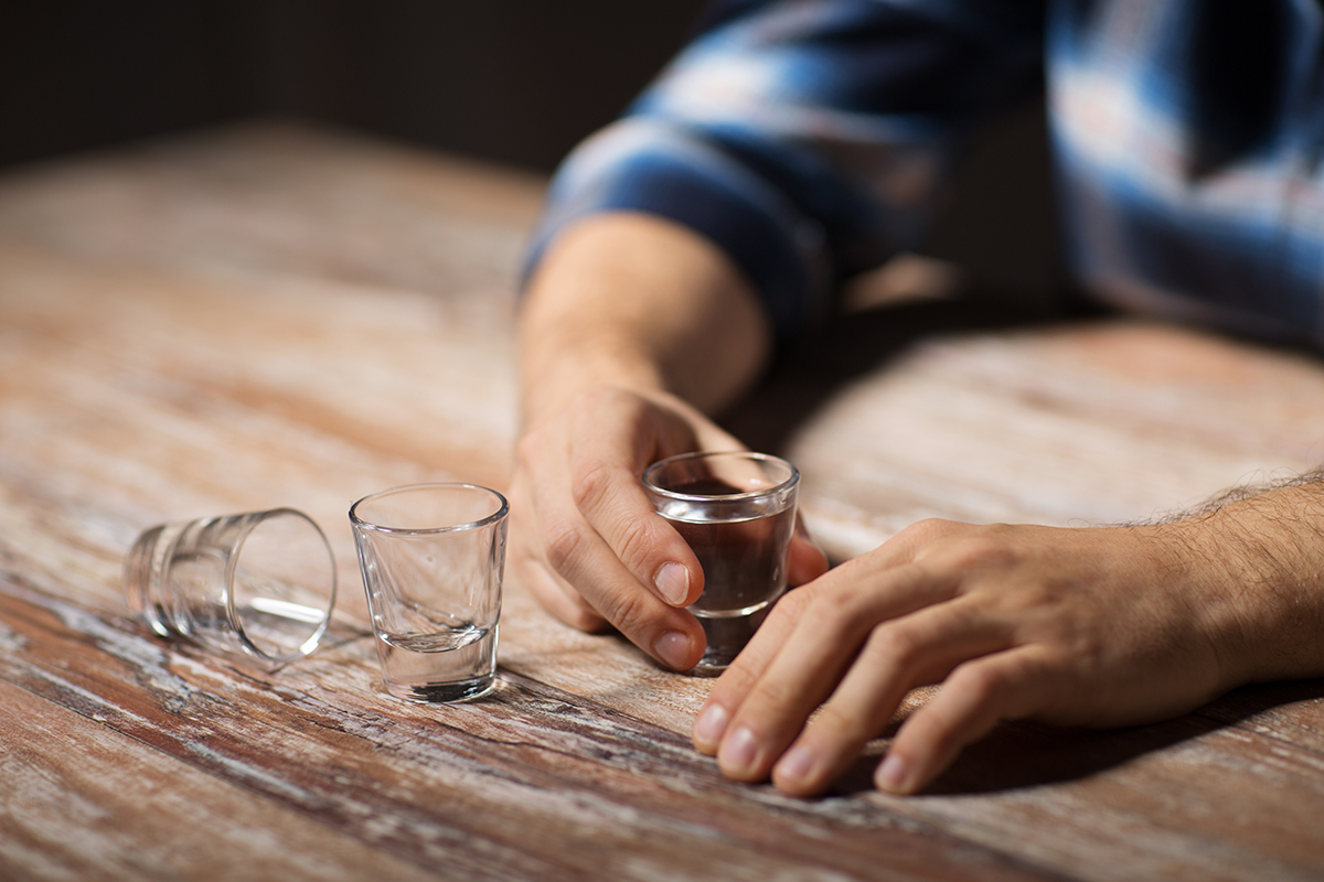 man holding shot glasses showing signs of alcohol addiction