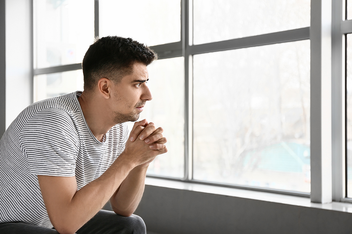 man looking out the window struggling with his addiction triggers
